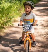 Young rider on an orange 12 Pro balance bike striding on a dirt trail