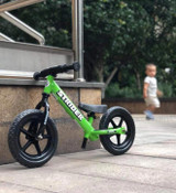 Side view of a green 12 Sport balance bike propped up against a concrete wall