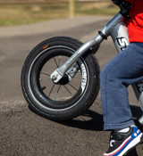 Close up of a Strider Carbon Fiber Wheel on the front frame of a silver 12 Pro balance bike