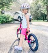 Child sits on a Funky Fuchsia Strider 14x bike while looking back and smiling