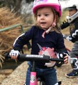 Young child on a pink Strider 12 Sport balance bike wearing the Strider Elbow and Knee Pad Set