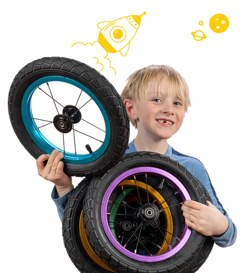 Smiling young boy holds Strider High-Traction Wheels in blue, purple, gold, and green.