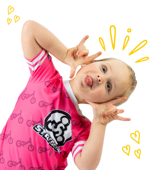 4-year-old girl wearing a pink 3T Strider Kids Jersey making a silly face for the camera and sticking her tongue out. Yellow doodles are drawn around her head.