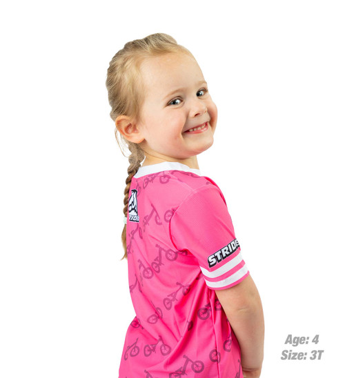 Girl age 4 wears a pink 3T Strider Kids Jersey with balance bike pattern across the back.