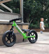 Side view of a green 12 Sport balance bike propped up against a concrete wall
