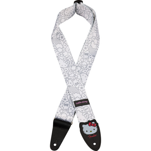 White guitar strap with a light gray Hello Kitty-themed pattern featuring various Sanrio characters and shapes. The strap has black leather ends, one of which displays a Hello Kitty face with a red bow and the Fender logo in red. A small pink tag near the center reads ‘Hello Kitty.’