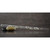 Transparent piccolo with white lily floral motif, resting horizontally on a brown surface and supported by a black stone and a beige stone.