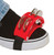A red plastic foot tambourine with metal jingles attached to the toe of a black and white sneaker using a black elastic strap.