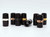 Eight black cylindrical clarinet barrels with metallic bands in silver, black, gold, and rose gold. One cylinder lies on its side; the rest stand upright on a flat surface.