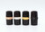 Four black cylindrical clarinet barrels with metallic bands in rose gold, silver, gold, and black nickel, arranged upright in a row, showcasing their color variations and sleek design.