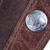 Close-up of a silver coin like embossed logo with an engraved buffalo on a brown leather guitar strap with visible stitching and two-tone textured leather.