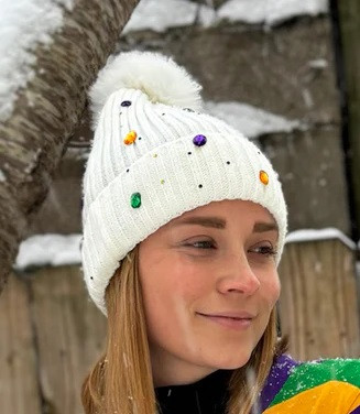 Mardi Gras Jeweled Beanie. Available in white or black, this soft beanie features a fluffy pom pom on top and is decorated with purple, green, and gold costume gems.