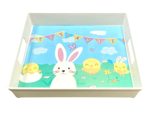 Easter Bunny Square Tray. The plastic square tray features handles on each side for easy carrying and serving up seasonal treats. Adorned with a print of a cartoon white bunny surrounded by three chicks, green grass, and flowers beneath a bright blue sky and colorful pennants, this tray adds a fun and festive touch to any Easter celebration. Measures 11in x 11in.
