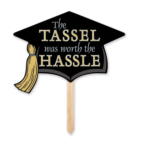 Grad Cap Yard Sign. Featuring a black cardstock graduation hat with a gold tassel, this sign is attached to a pine stake. The phrase "The TASSEL was worth the HASSLE" is displayed in silver and gold lettering. Measures 13in x 17.5in. 24in tall with stake.