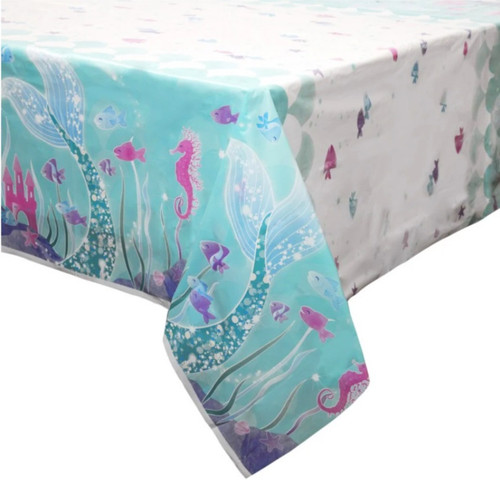 Mermaid Plastic Table Cover. This white rectangular plastic cover features a pattern of colorful fish. The center fades into the borders with blue mermaid scales, featuring a repeating pattern of an underwater scene with colorful fish, pink sandcastles, and mermaid tails. Measures 54in x 84in.