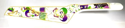 Mardi Gras Cake Server. This white plastic server is decorated with mardi gras iconography such as masks, instruments, and confetti in purple, green, and gold. Measures 10in x 2.25in.