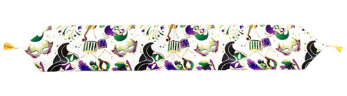 All Mardi Gras Table Runner. This white cotton fabric runner features a printed pattern of Mardi Gras imagery such as masks, confetti, and instruments in purple, green and gold, with yellow tassels on the ends. The underside is solid purple fabric. Measures 12.25in x 71in.