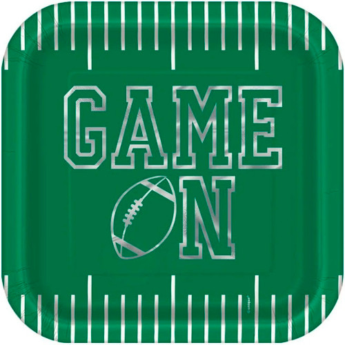 Game Face Football Luncheon Plates. These green, square shaped paper plates feature white lines, like those on a football field, on the top and bottom edges. Centered is "GAME ON" in silver foil text with a football silhouette in the place of the "O." Package includes 8 count plates measuring 8.75in.