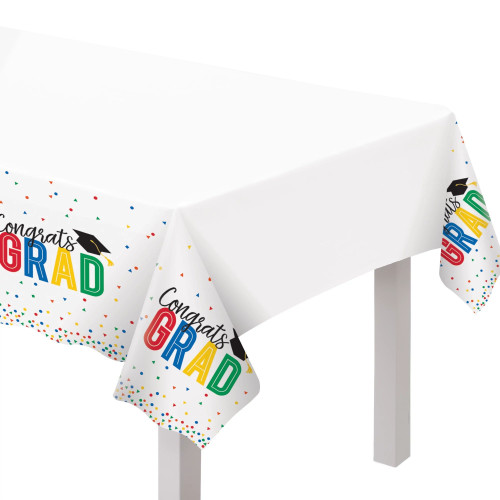 Colorful Future Grad Plastic Tablecover. This white, rectangular, scalloped edge plastic tablecover has an edge decorated with multicolor confetti. A repeating pattern features "Congrats" in black script over "GRAD" in big colorful letters, topped with a black grad cap. Measures 54in x 102in.