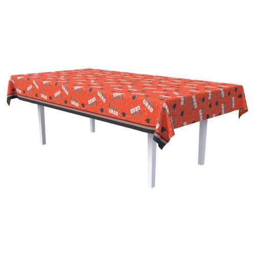Congrats Grad Plastic Tablecover - Orange. This rectangular plastic tablecover features an orange background, decorated with a pattern of white and black star confetti, along with black graduation caps and groups of "Congrats" in black script over "GRAD" in white block text. Measures 54in x 108in.