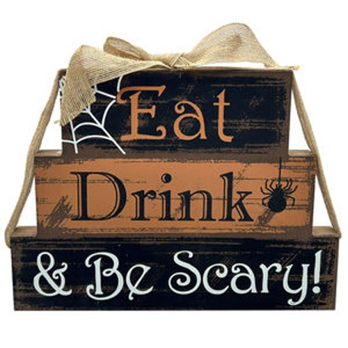Eat Drink & Be Scary Block Tabletop Stand. This decoration is made of three stacked weathered looking blocks increasing in size in black, orange, and black again, topped with a burlap bow, and featuring the text "Eat Drink & Be Scary!" Measures 11.75in wide x 9in tall x 1in thick.