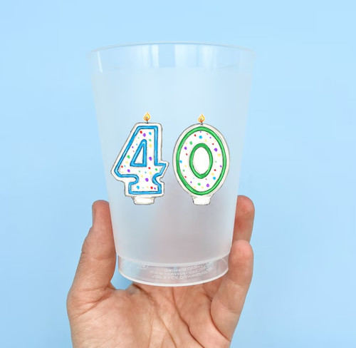 Age 40 Party Cups. These frosted clear plastic cups feature a painterly illustration of lit number candles "4" and "0" that are white with multicolor dots and blue and green outlines. Package includes 6 count 16oz cups, about 4in tall.