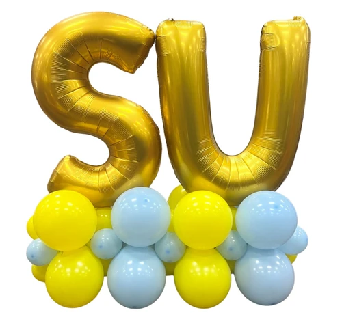 SU Balloon Floor Decoration. This balloon decoration stands approximately 50in tall x 50in long and features yellow and pastel blue 12in and 5in latex balloons topped with "SU" in gold foil balloons.