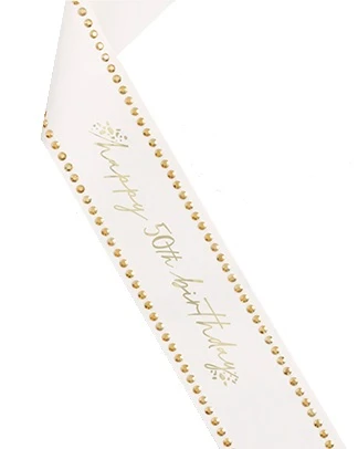 Paper 50th Birthday Sash with Gold Rhinestones. This white cardstock paper sash features "happy 50th birthday" in gold foil script, accented by cluster of gold foil spots framing the text and gold acrylic rhinestones along the edges. One size fits most.