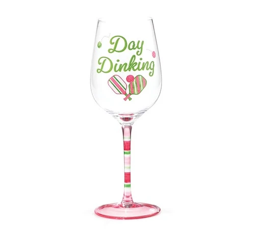 Stemmed Wine Glass - Day Dinking. This wine glass features a decal design of "Day Dinking" in green script, accented by pink and green pickleballs and paddles. The stem has pink and green stripes varied thickness with a pink base.. Measures 9in tall with a 2.5in opening, holds up to 12oz. Hand wash only. Arrives in a clear, cylindrical gift box with a lime green base and a pink bow.