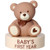 Beary First Year Decoset. This plastic topper features a brown teddy bear on an off white platform with "BABY'S FIRST YEAR" in brown text. Contained in the platform are several plastic disc with text such as "WE CAN bearly WAIT," "hello WORLD," as well as milestones, including one, two, three, four, five, six, seven, eight, nine, ten, eleven months, and one year. Bear measures 2.8in x 2.05in x 3.05in. Container measures 3.45in x .85in. 14 count discs measure 3.14in x 3.2in x .1in.