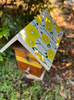 Garden beehive with a white roof hand-painted with bright yellow flowers and green stems.