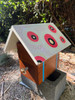 Wooden beehive topped with a hand-painted roof featuring bold pink circular patterns.