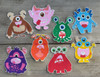 Fully coloured POSCA Colour In Monster Cards showing eight playful monster characters in bright colours, arranged on a wooden surface.