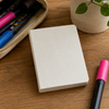 Closed blank mini painting book with textured white cover beside POSCA markers on a wooden creative workspace