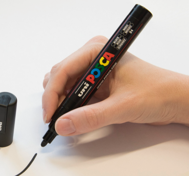 Hand using POSCA PC-5M marker to draw clean lines on a smooth white surface