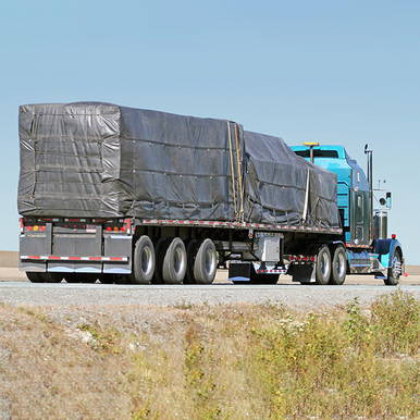 24' x 27' Lumber Tarp, 2 Flap, covering large cargo on a flatbed truck, providing protection against weather.