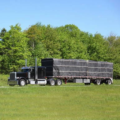 24' x 30' Lumber Tarp, 2 Flap, black heavy-duty tarp covering cargo on truck, outdoor scene with green trees and blue sky in background.