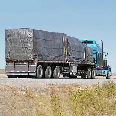 24' x 18' Lumber Tarp, 1 Flap, black tarp covering a flatbed truck transporting lumber on an open road under a clear blue sky.