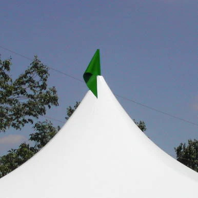 Green Pole Flag, vibrant green flag attached to a tall pole at the top of a white tent peak against a blue sky with trees in the background.