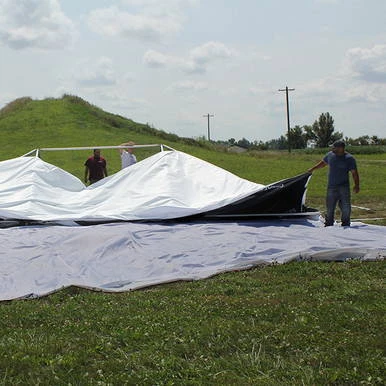 35' x 35' Polyester Drop Cloth, image shows workers setting up or adjusting a large white drop cloth outdoors on grassy terrain with a hill and power lines in the background.