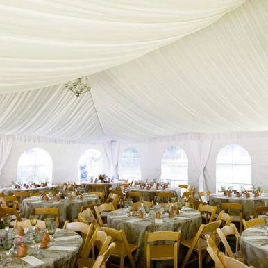 Celina Tent Frame Tent Liner 30' x 20' Mid, elegant white interior of a large event tent with draped fabric ceiling and arranged tables and chairs for a banquet or wedding reception.