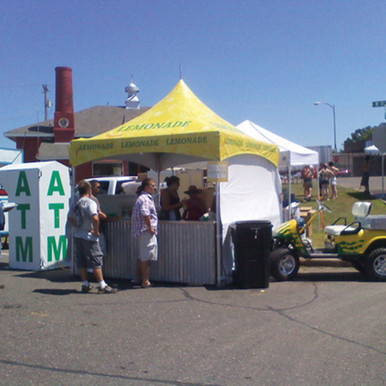 Celina Tent 10' x 10' Pinnacle Series High Peak Frame Tent / Cross Cable Marquee, complete setup at outdoor event with people gathered around and a yellow and white canopy.