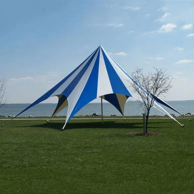 52' TP Series Hexagon Tent, Complete, outdoor event tent with blue and white striped canopy and supporting stakes on a grassy area near a body of water.