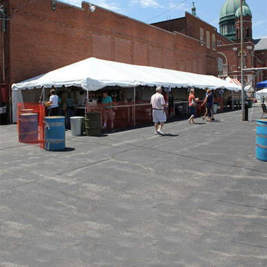20' x 80' Classic Series Frame Tent, Sectional Tent Top, Complete, shown as a large white banquet tent set up outdoors with people walking nearby, in an urban area with brick buildings and a church dome in the background.