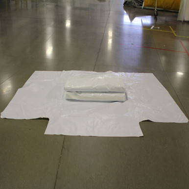 60" x 100" Wrap Around Bag, large white plastic wrap spread out on the floor with a smaller white package in the center.