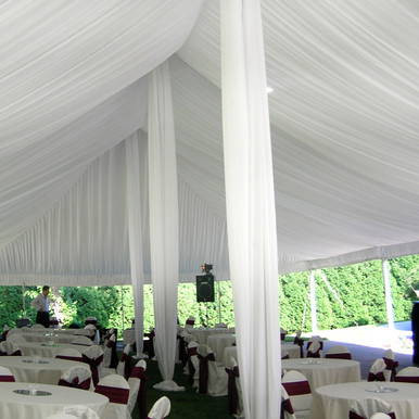 Center Pole Drape - 18' , interior view of event tent with tall supporting pole draped with white fabric and banquet tables set up underneath.