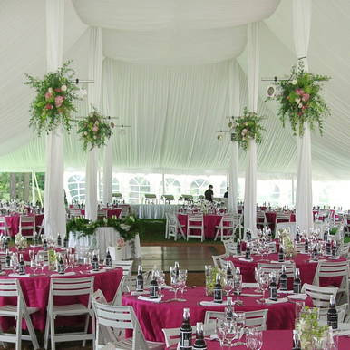 Center Pole Drape - 18' , elegant event tent with white drapes and floral decorations, set up for a formal banquet with pink tablecloths and white chairs.