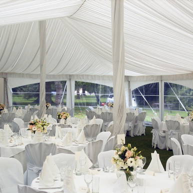 Center Pole Drape - 17' , interior view of wedding or event tent with elegant draped fabric ceiling and round tables with white tablecloths and floral centerpieces.