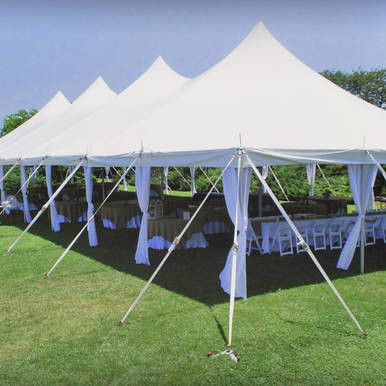 7' x 40" Leg Drape with Sash, white event tent with draped legs and sashes on a grassy outdoor setting under blue sky.
