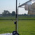 12' Frame Tent Jack, image showing a portable tent jack with wheels and a vertical metal pole supporting a tent canopy in an outdoor field setting.